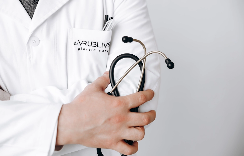 Професійний пластичний хірург клініки dr. VRUBLYVSKY — на фото лікар у медичному халаті з логотипом клініки та стетоскопом у руках. 